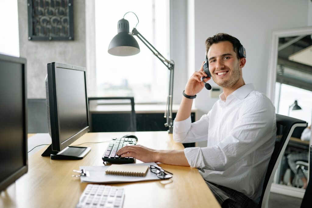 pexels photo 8867374 8867374 Smiling call center agent working at a desk with a headset and computer in a modern office.